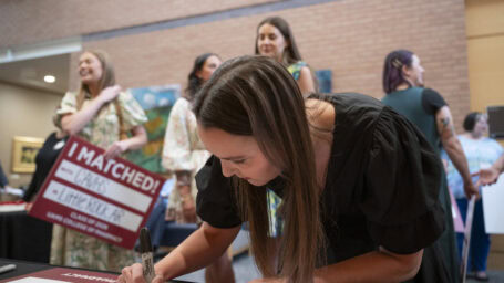 a woman bends down to fill out her Match Day poster