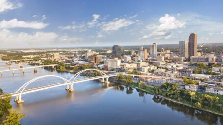 An aerial view of the Arkansas river with several bridges spanning to downtown Little Rock where skyscrapers cover over downtown.