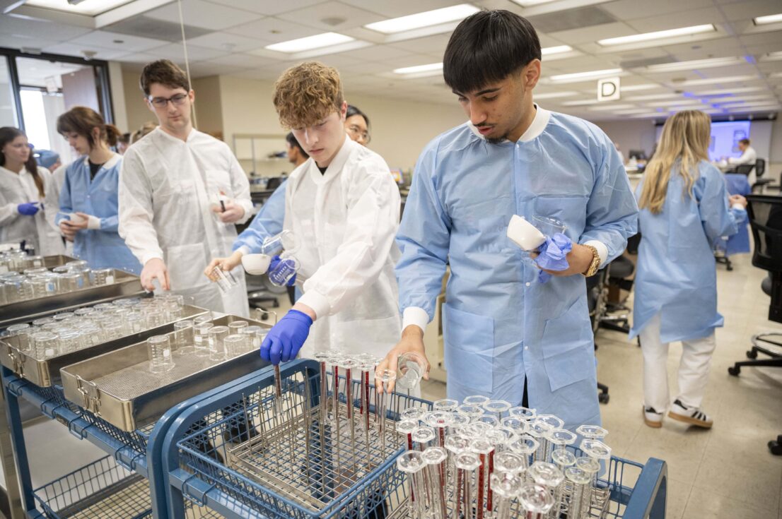 A student wearing a blue gown looks at pharmacy equipment