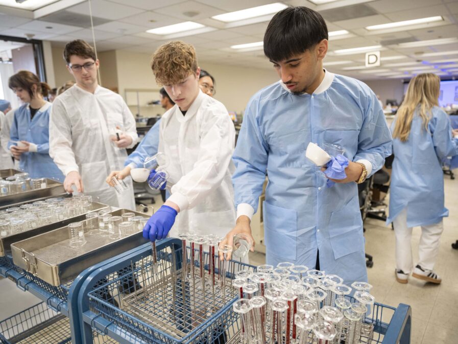 A student wearing a blue gown looks at pharmacy equipment